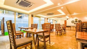 A dining area with wooden tables and chairs, large windows, and a view of buildings outside. - FabHotel Casa Kiara With Pool Side Bar, Calangute (Calangute)