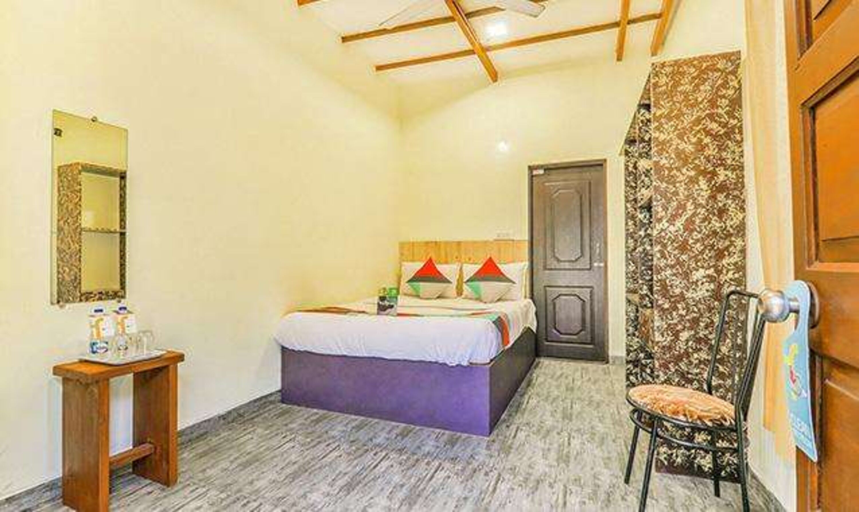 A bedroom with a bed, a chair, a small table, and a door.