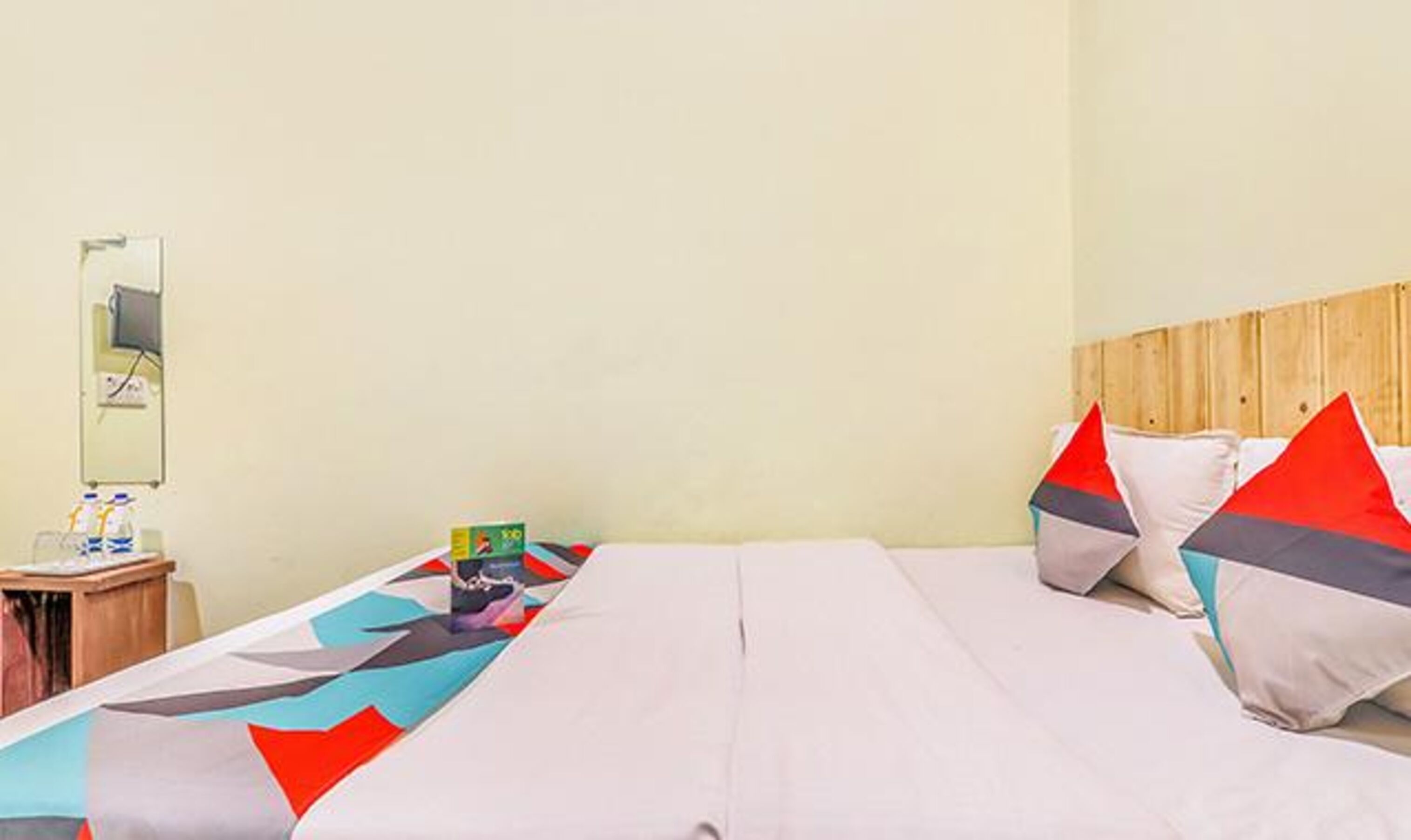 Una habitación de hotel con cama, almohadas, una mesita de noche y un espejo.