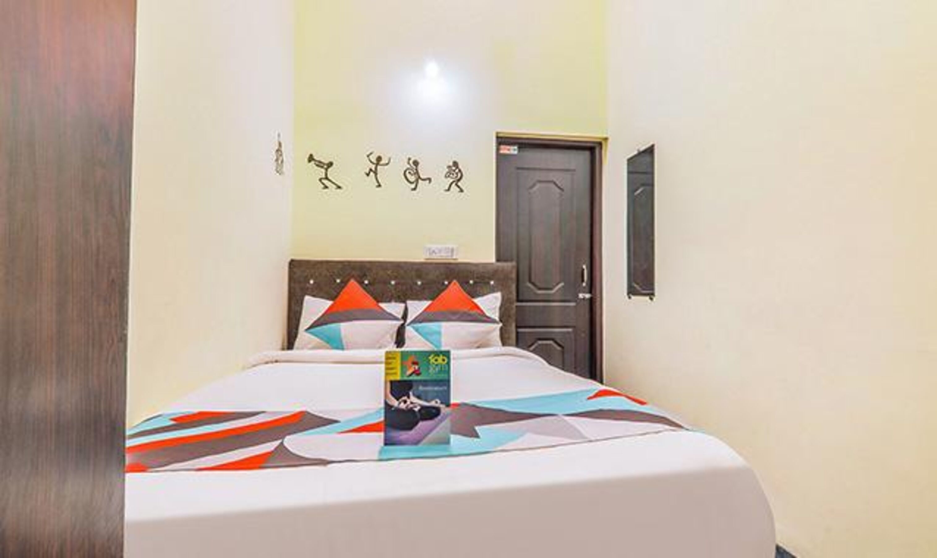 Uma cama bem arrumada com um edredom e almofadas de padrão geométrico colorido, uma porta de madeira e um painel decorativo simples na parede.
