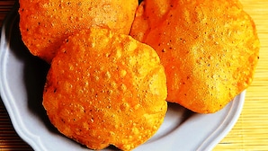Tres porciones redondas y doradas, fritas, sobre un plato blanco, con un tazón pequeño de vegetales variados al fondo.