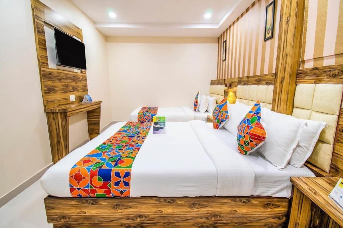 A hotel room with a wooden headboard, a flat-screen TV mounted on the wall, a bed with a colorful geometric-patterned bedspread, and a bedside table with a lamp.