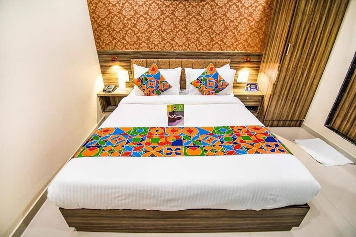 A hotel room with a bed, two bedside tables, a nightstand, a patterned wall, and a curtain.