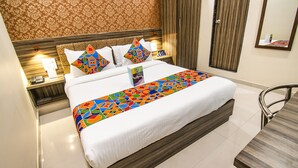 A hotel room with a large bed, a wooden headboard, a bedside table with a lamp, and a mirror on the wall. - FabHotel Orange Suites (Mumbai)