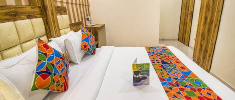 A hotel room with a large bed, a wooden headboard, a small bedside table with a water bottle, and a colorful bed runner.