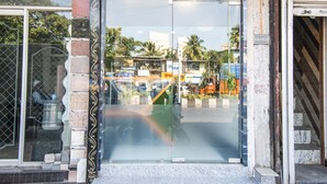 The entrance to Hotel Orange Suite with a glass door, a visible parking area, and a street view with buildings and palm trees. - FabHotel Orange Suites (Mumbai)