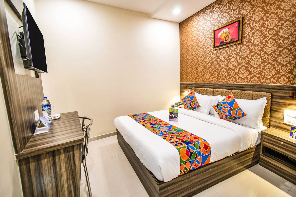 A hotel room with a bed, a TV, a desk, and a wall with a patterned wallpaper.