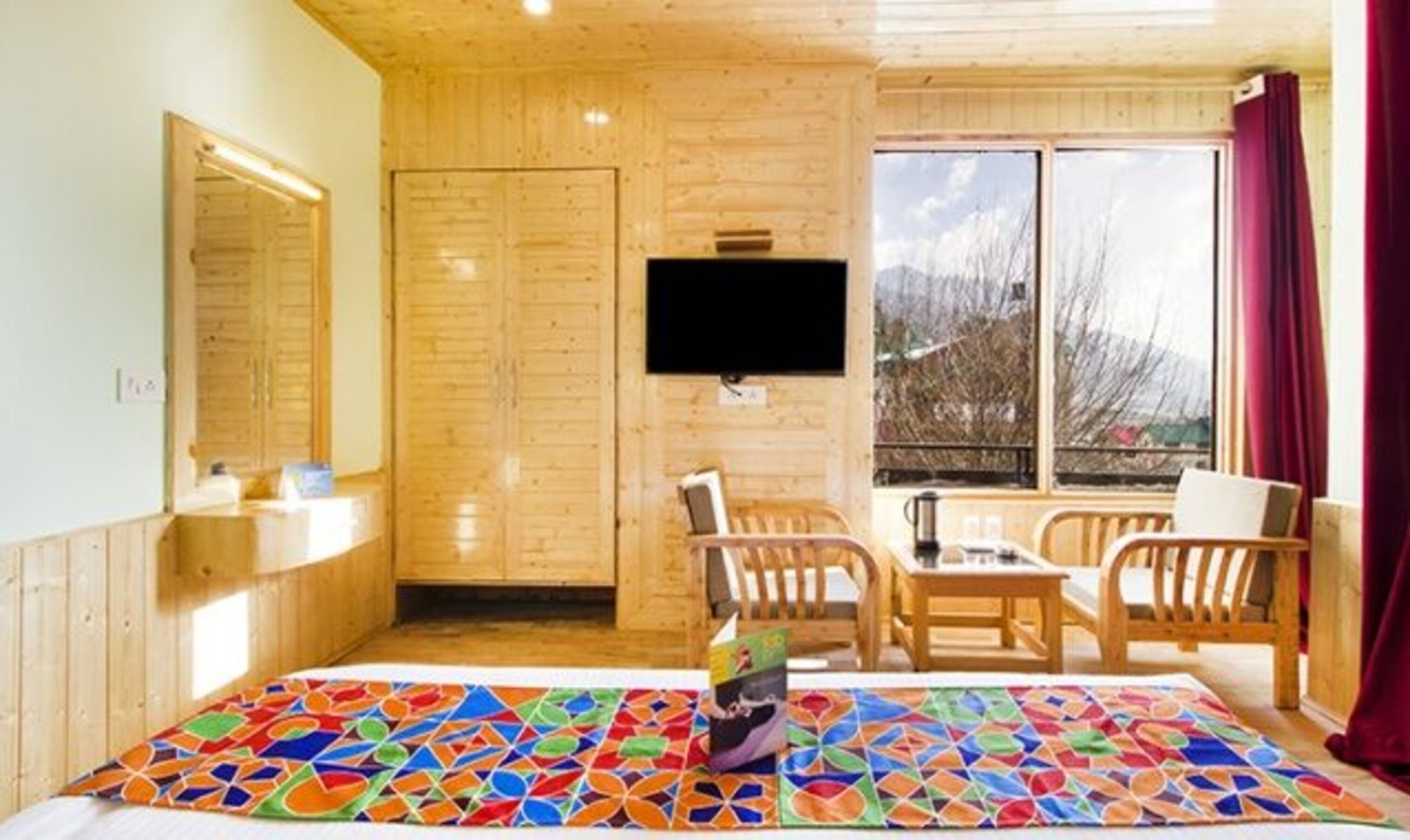 A cozy room with wooden walls, a flat-screen TV, a dining table with chairs, and a colorful rug.