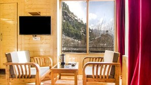 A wooden cabin interior with two wooden chairs, a small table, a mounted TV, and a window with a view of a mountainous landscape. - FabHotel Shami Inn (Manali)