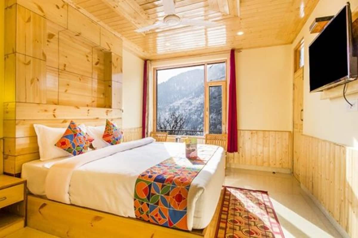Una habitación de cabaña de madera con una cama, una mesita de noche, un ventanal con vistas a montañas nevadas y un televisor montado.