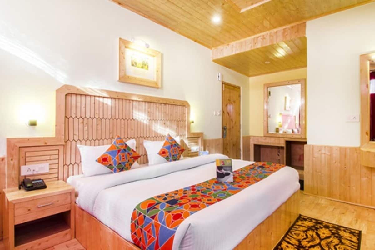 Habitación de hotel con cabecera de madera, cama con ropa de cama colorida, mesita de noche con teléfono, espejo y suelo de madera.