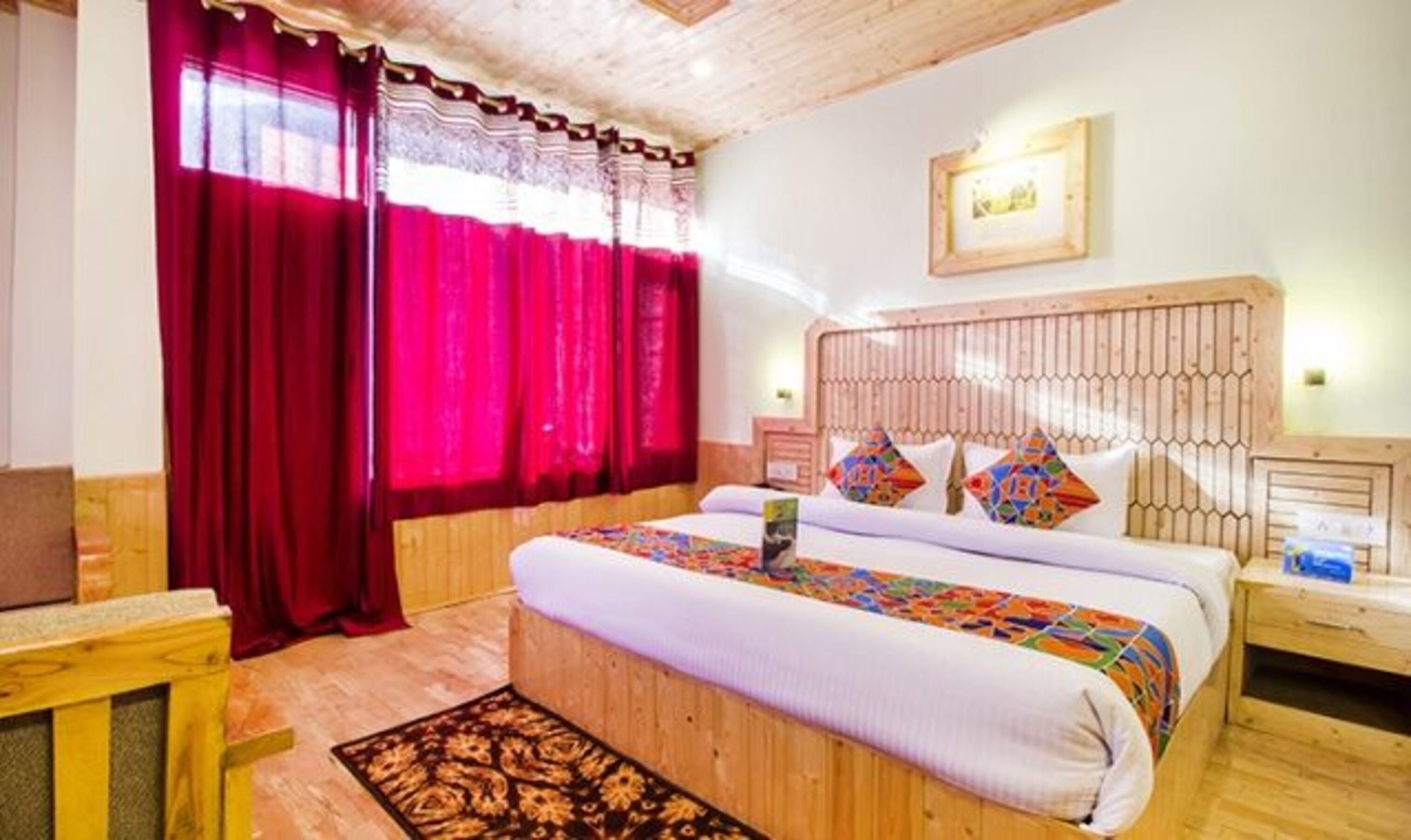 A bedroom with a wooden headboard, a bed with colorful pillows, a nightstand, and a red curtain.