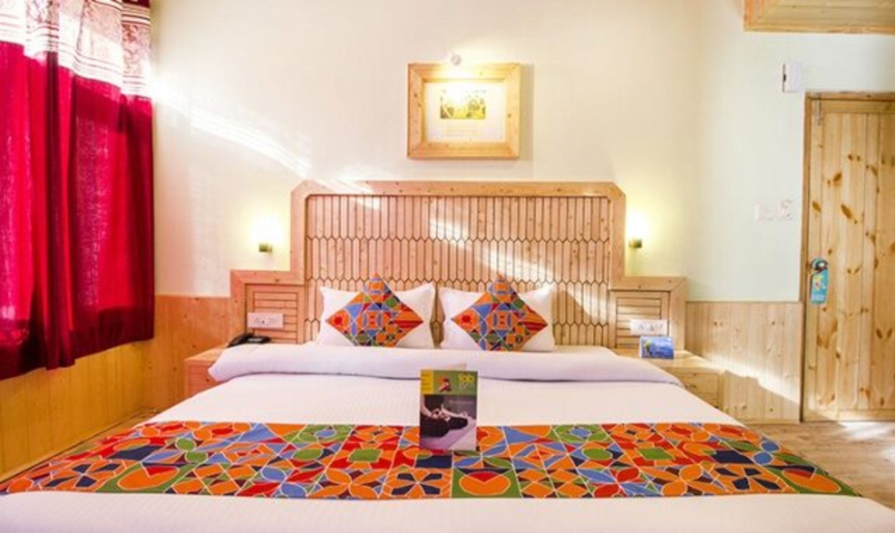 A hotel room with a wooden headboard, a colorful bedspread, and a framed picture on the wall.