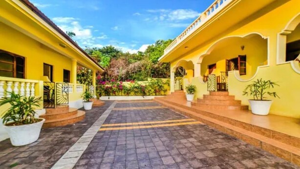 A courtyard with yellow buildings, potted plants, and a paved walkway. - FabHotel La Pablo - Nr. Chapora Fort (Vagator)