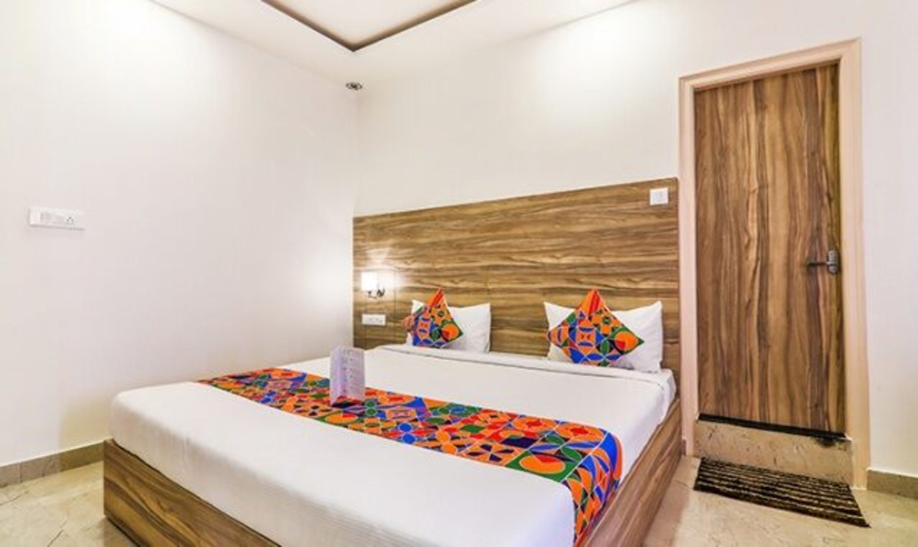 A hotel room with a wooden headboard, a bed with colorful bedding, and a wooden door.