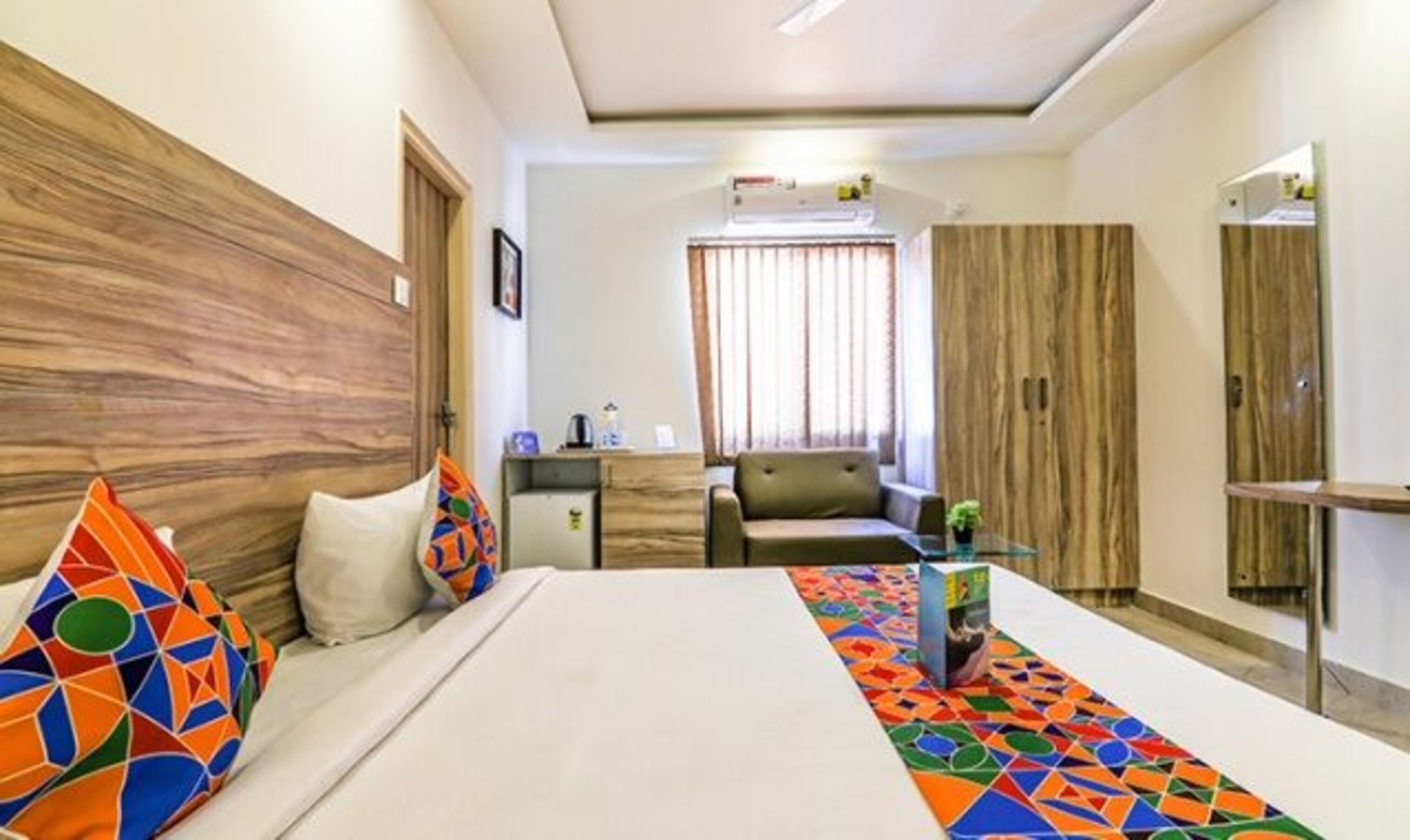 Une chambre d’hôtel comprenant un lit, un bureau, une chaise, une armoire et une fenêtre avec des rideaux.