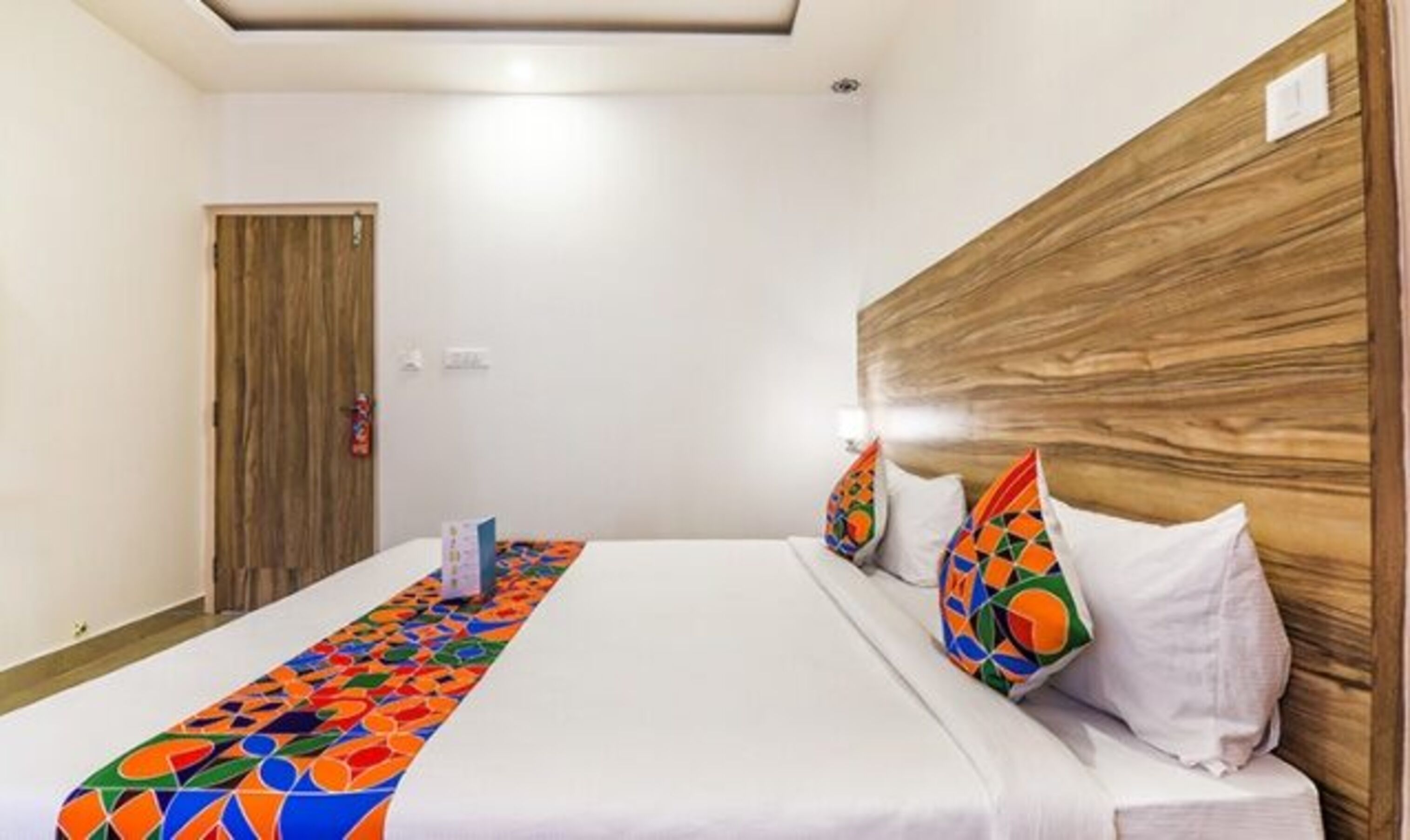 Une chambre d’hôtel avec une tête de lit en bois, une couvre-lit blanche et des coussins colorés.