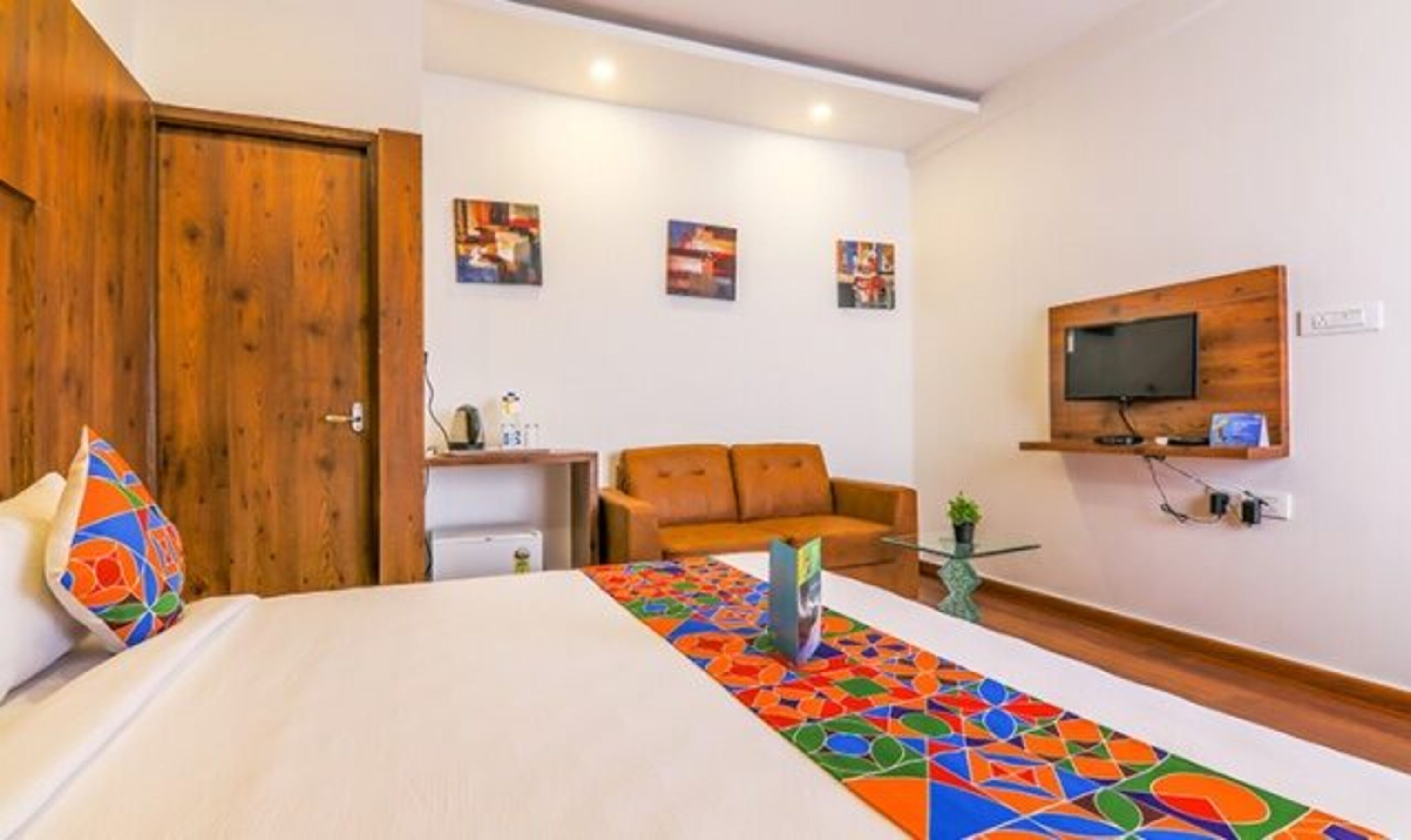 Habitación de hotel con cama, sofá, televisor montado en la pared y una mesita con una planta.