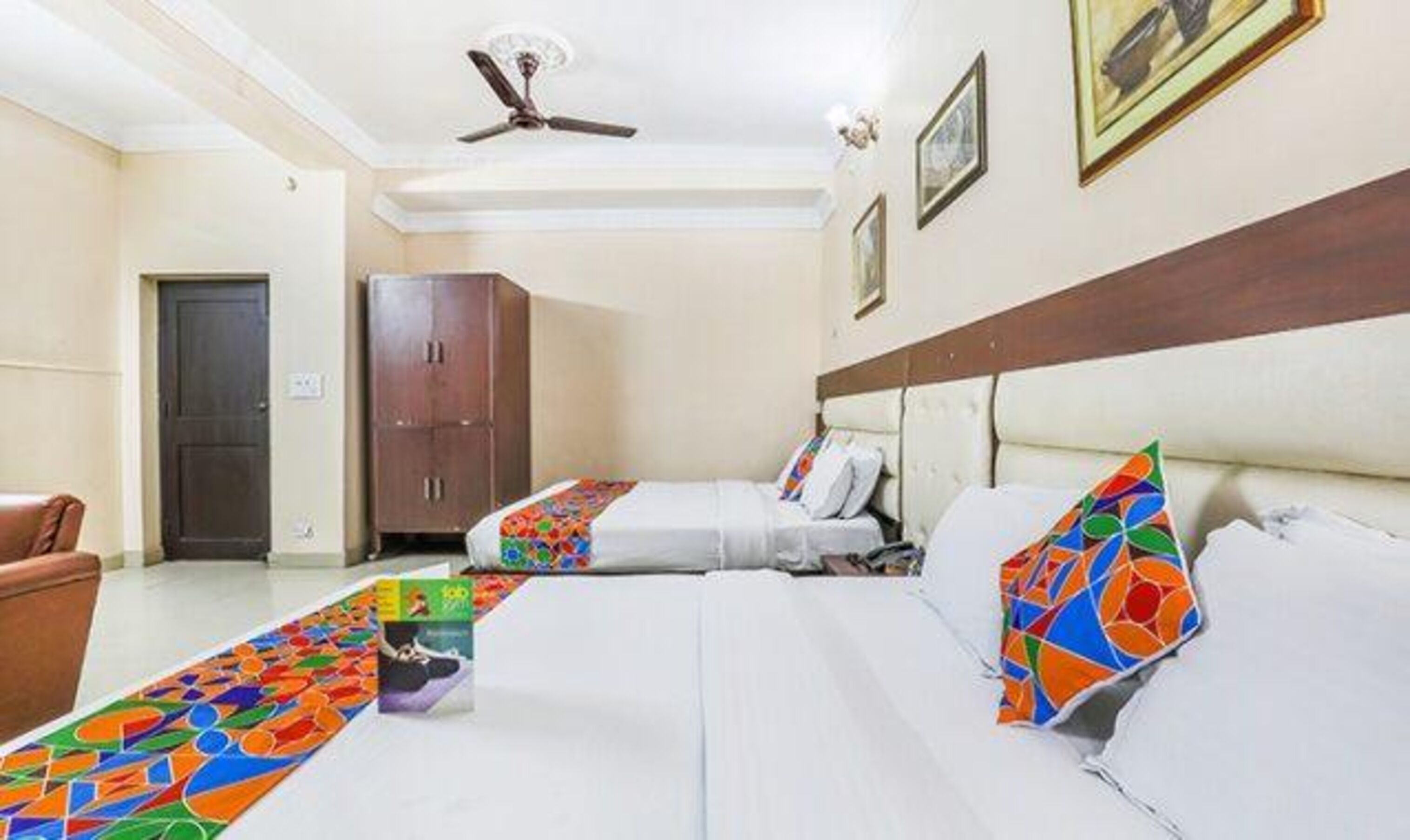 A hotel room with two beds, a wardrobe, a ceiling fan, and a door.