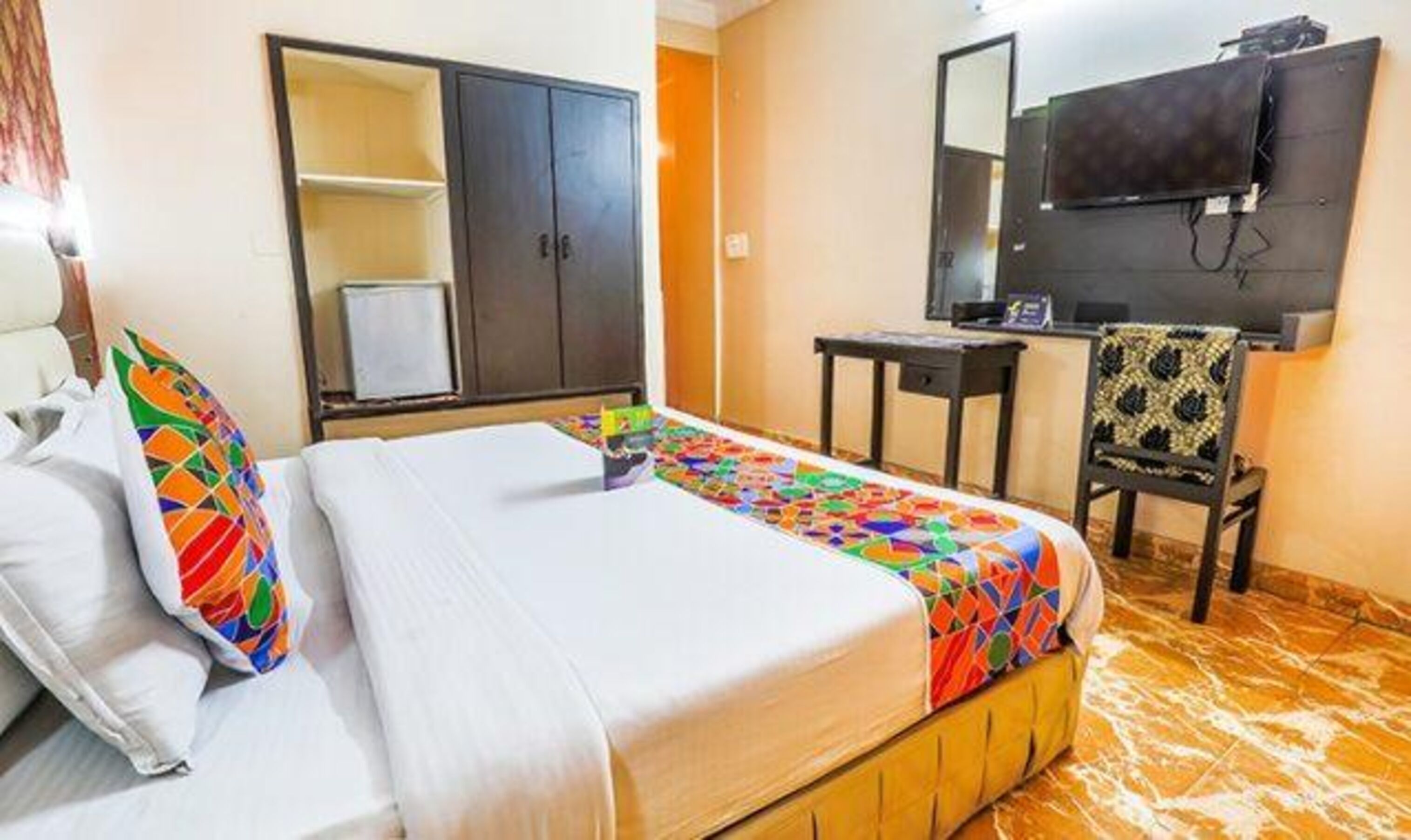 A hotel room with a bed, a wardrobe, a desk, a chair, and a television.