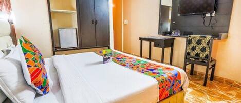 A hotel room with a bed, a wardrobe, a desk, a chair, and a television.