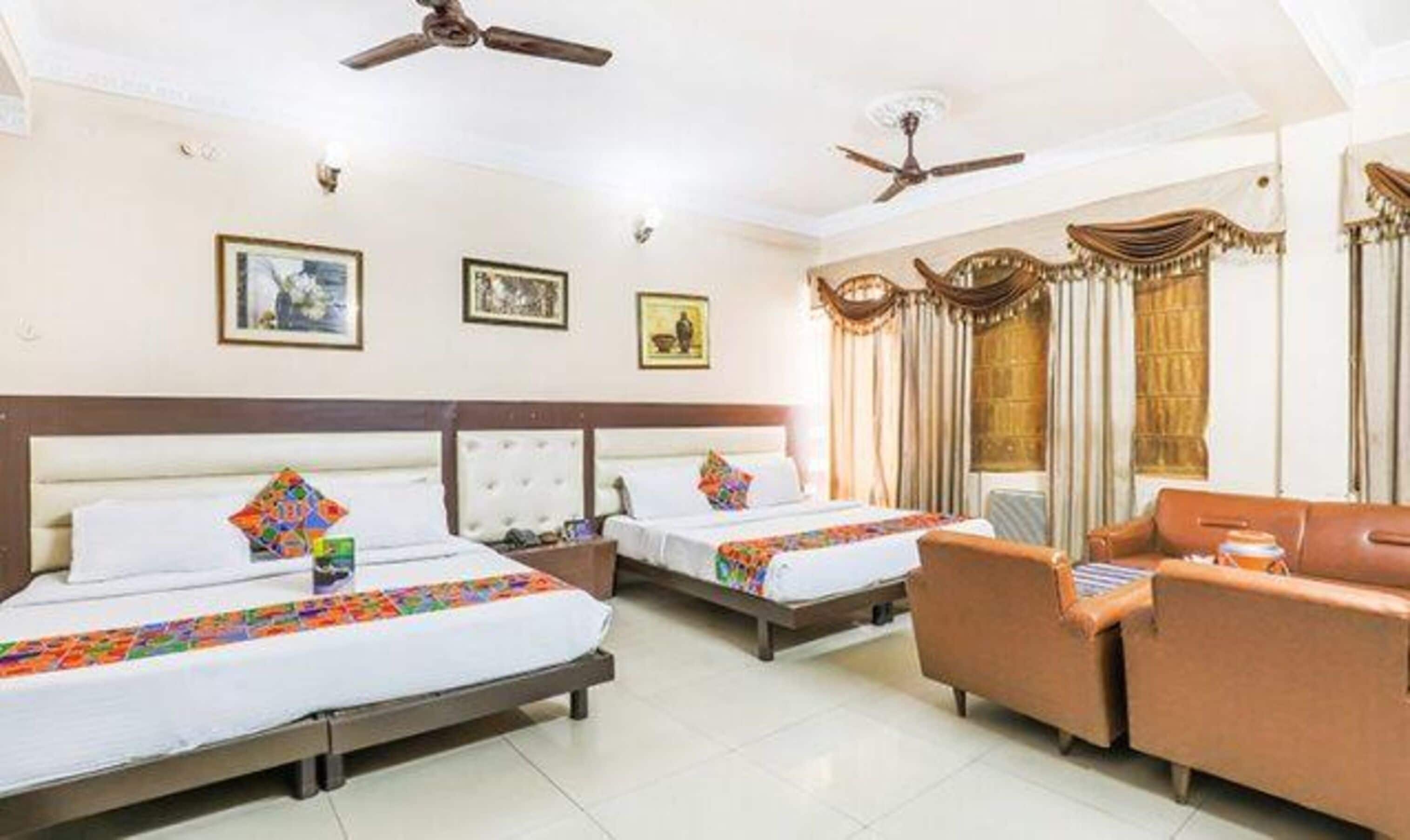 Quarto de hotel com duas camas, um sofá e ventiladores de teto.