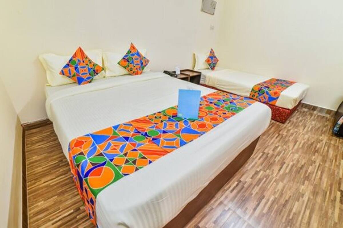 A hotel room with a large bed, two smaller beds, a wooden floor, and a colorful geometric-patterned bedspread.