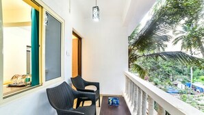 A balcony with two chairs and a small table, overlooking a lush garden with palm trees. - FabHotel K7 Trends With Pool, Baga Beach (Calangute)