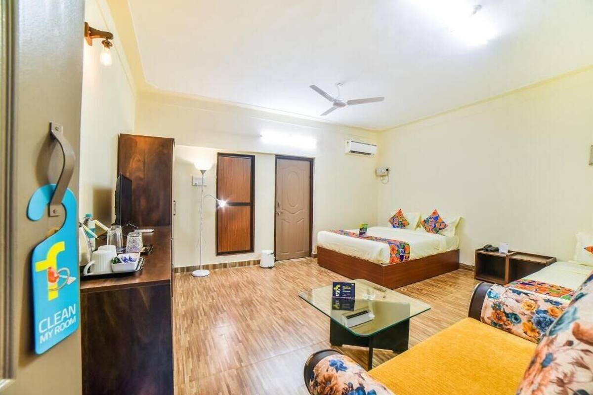 A hotel room with a bed, a sofa, a glass coffee table, a desk with a computer, a ceiling fan, and an air conditioning unit.