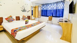 A hotel room with a large bed, a desk, a chair, a television, and a window with blue curtains. - FabExpress Karishma - Shivaji Nagar, Pune (Pune)