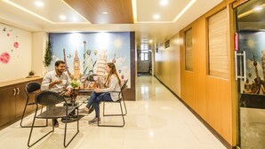 A hotel lobby with a reception desk, two chairs, a wall mural with famous landmarks, and a wooden panel wall. - FabExpress Karishma - Shivaji Nagar, Pune (Pune)