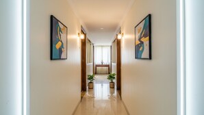 A hallway with two framed abstract paintings on the walls, a wooden bench, and potted plants at the end. - FabExpress Karishma - Shivaji Nagar, Pune (Pune)