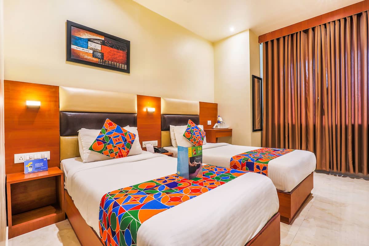 A hotel room with two beds, each with a colorful geometric-patterned bedspread, wooden headboards, and a wall-mounted painting.