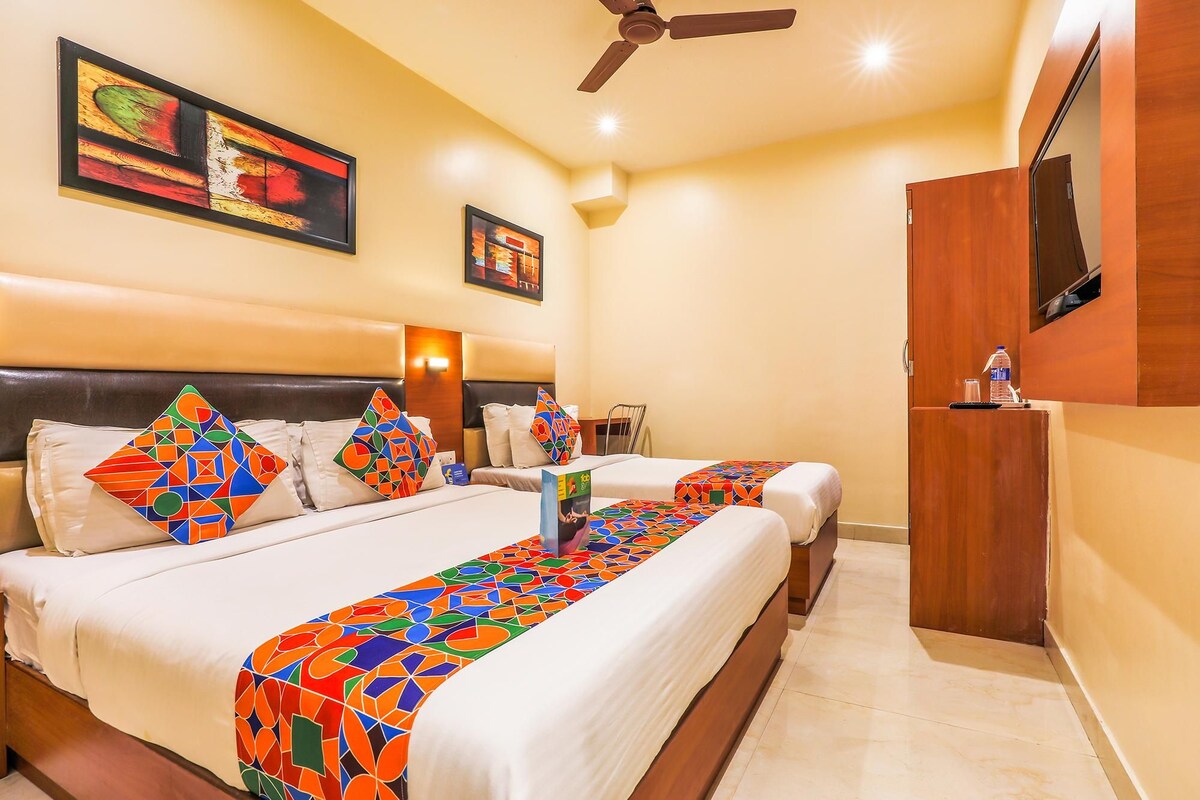 A hotel room with two beds, a ceiling fan, artwork on the walls, and a TV mounted on the wall.
