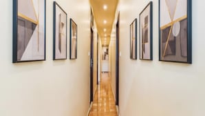 Un pasillo con arte abstracto enmarcados en las paredes, piso de madera pulida e iluminación empotrada en el techo.