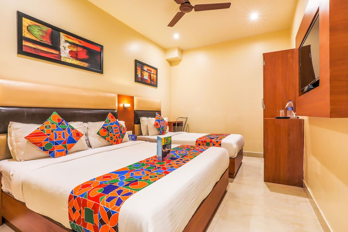 A hotel room with two beds, a ceiling fan, a TV, and artwork on the walls.
