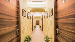 A hotel hallway with wooden paneling, numbered doors, potted plants, and framed artwork on the walls. - Fabhotel Landmark Residency (Navi Mumbai)