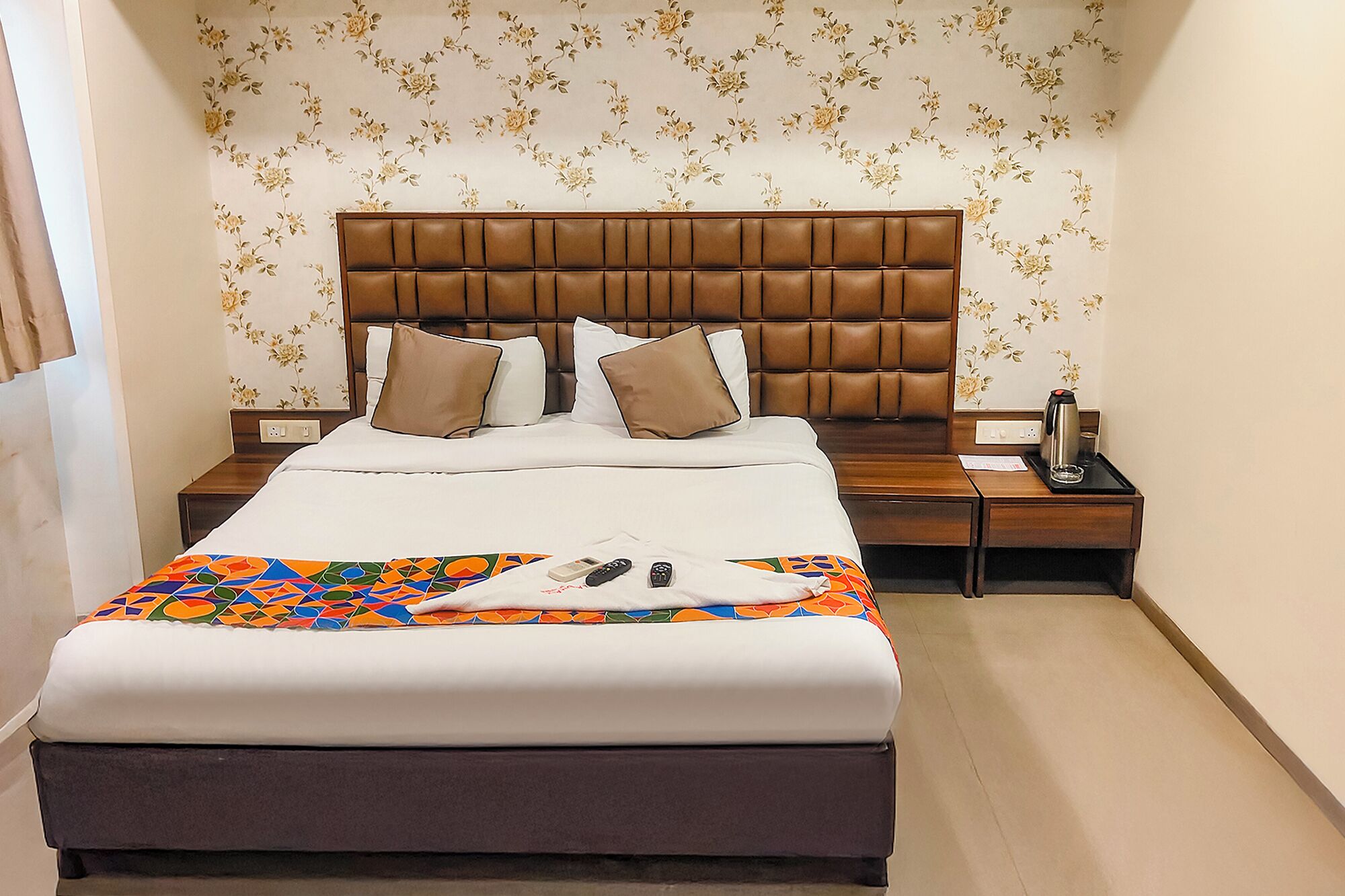 A hotel room with a large bed, a wooden headboard, and a floral wallpaper design.