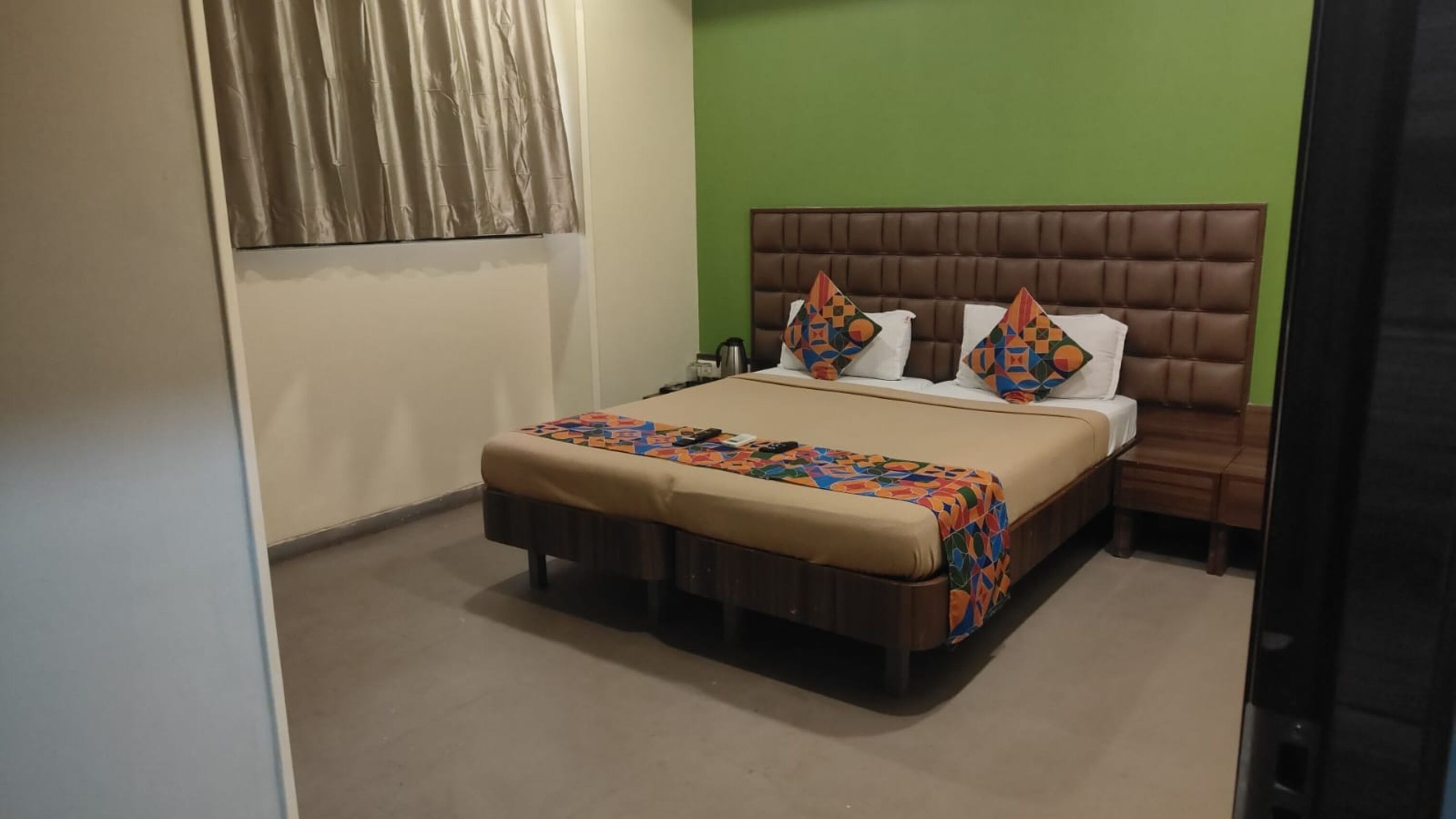 A hotel room with a bed, a nightstand, a green wall, and a window with curtains.