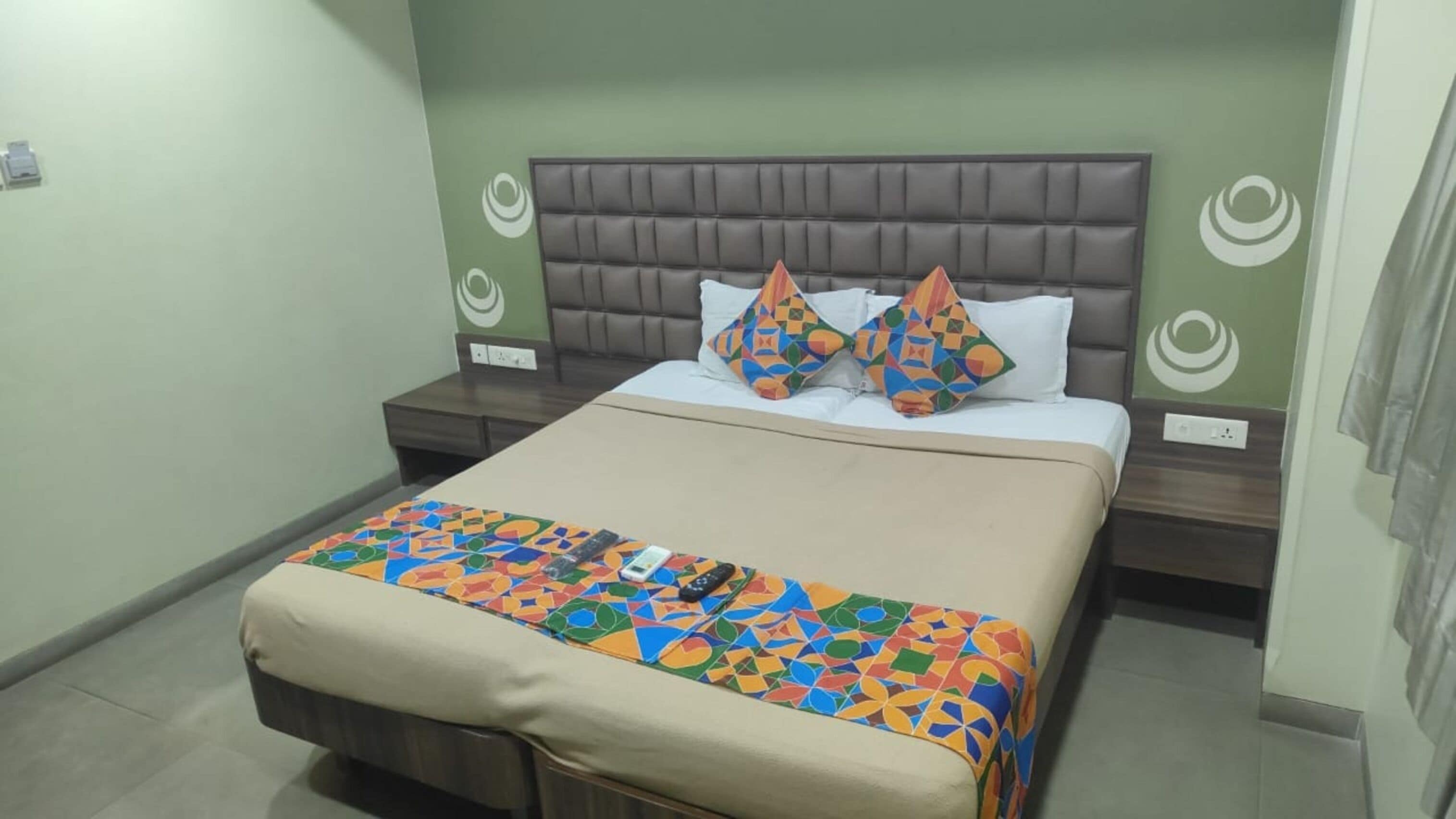 Una cama bien hecha con una colcha estampada, un cabecero tapizado en marrón y dos almohadas decorativas.