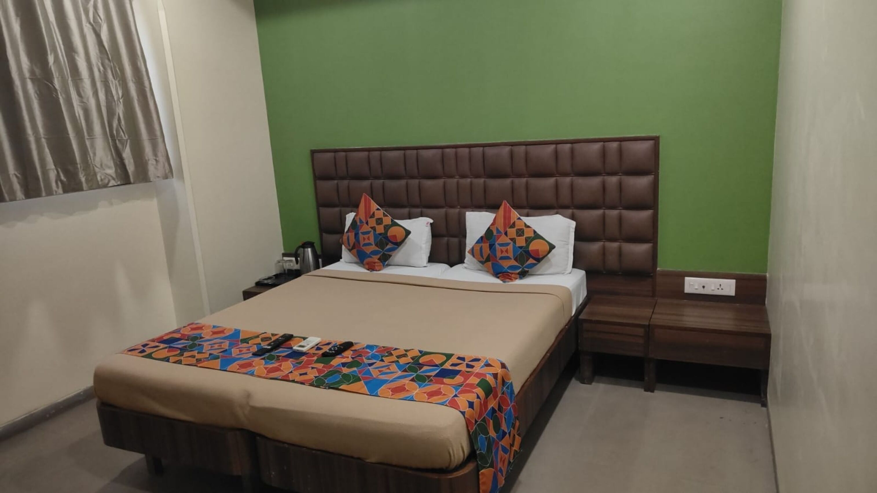 Habitación de hotel con una cama, una mesita de noche y una pared verde.