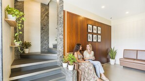 A modern interior with a staircase, wooden panel wall, framed botanical artwork, and a seating area with a sofa. - Fabhotel Landmark Residency (Navi Mumbai)