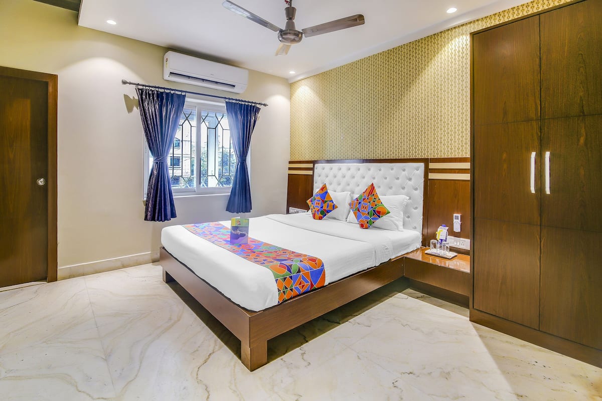 A bedroom with a bed, a wardrobe, a nightstand, a window with curtains, and an air conditioning unit.
