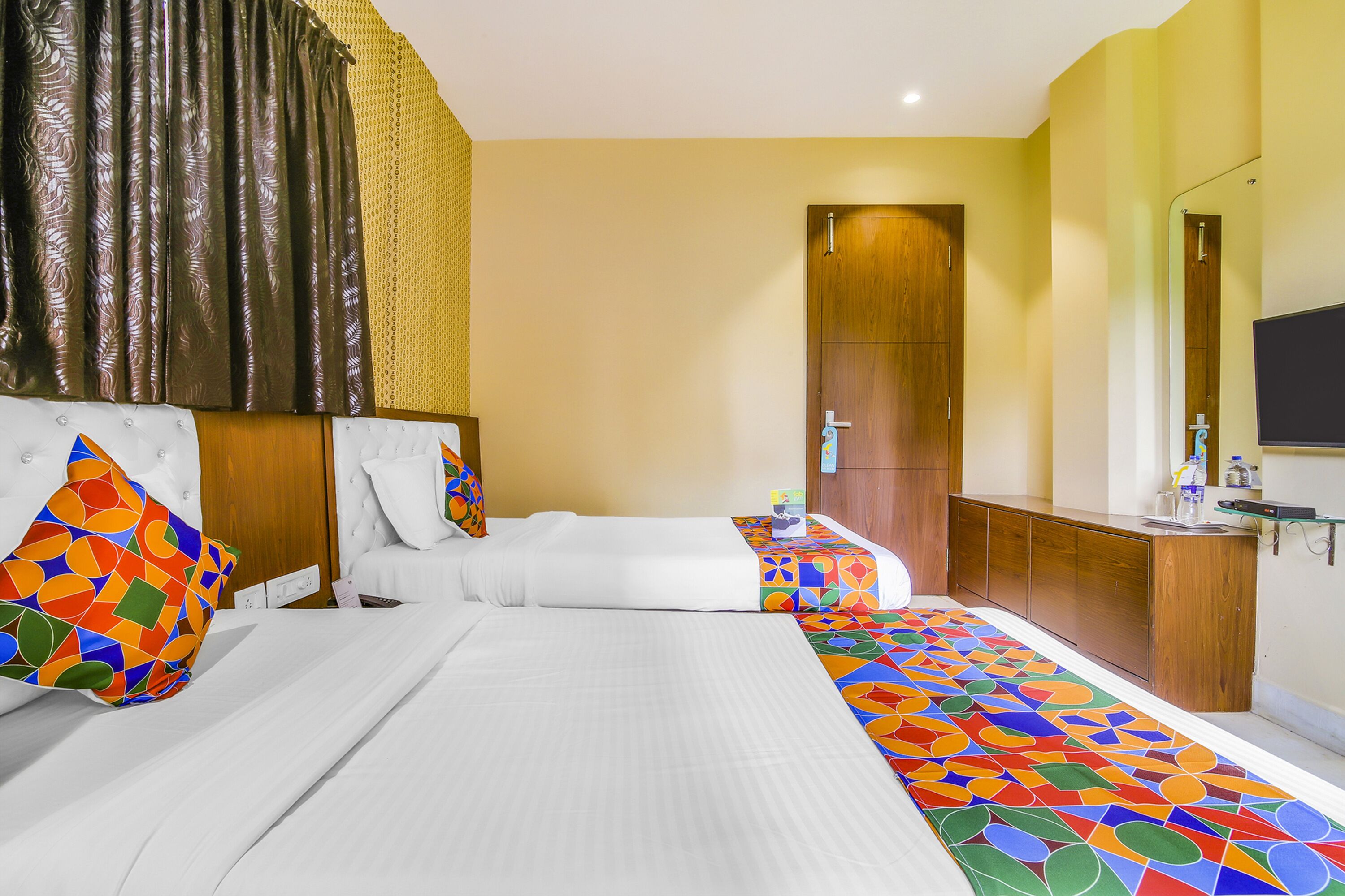 A hotel room with two beds, a wooden wardrobe, a bathroom with a mirror, and a TV.