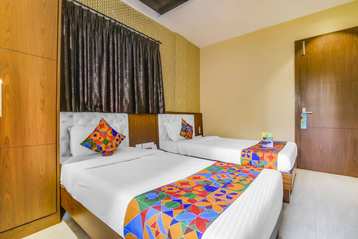 A hotel room with two beds, a wooden wardrobe, a curtain, and a door.