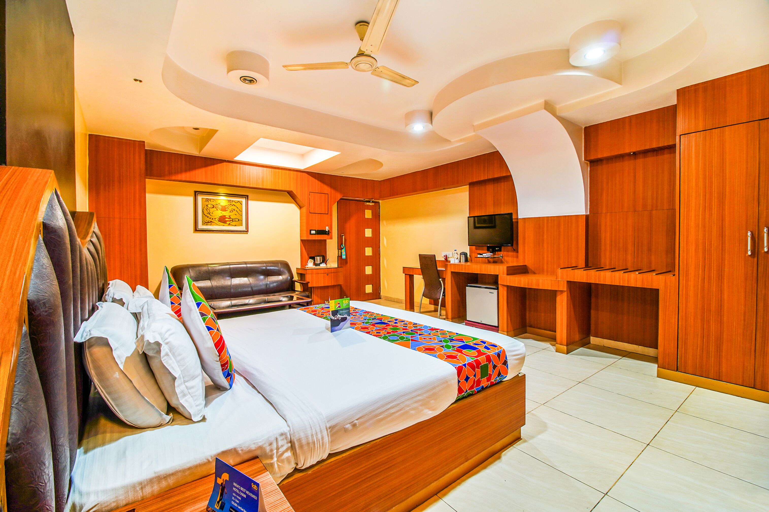 A hotel room with a bed, a desk, a television, and wooden cabinets.