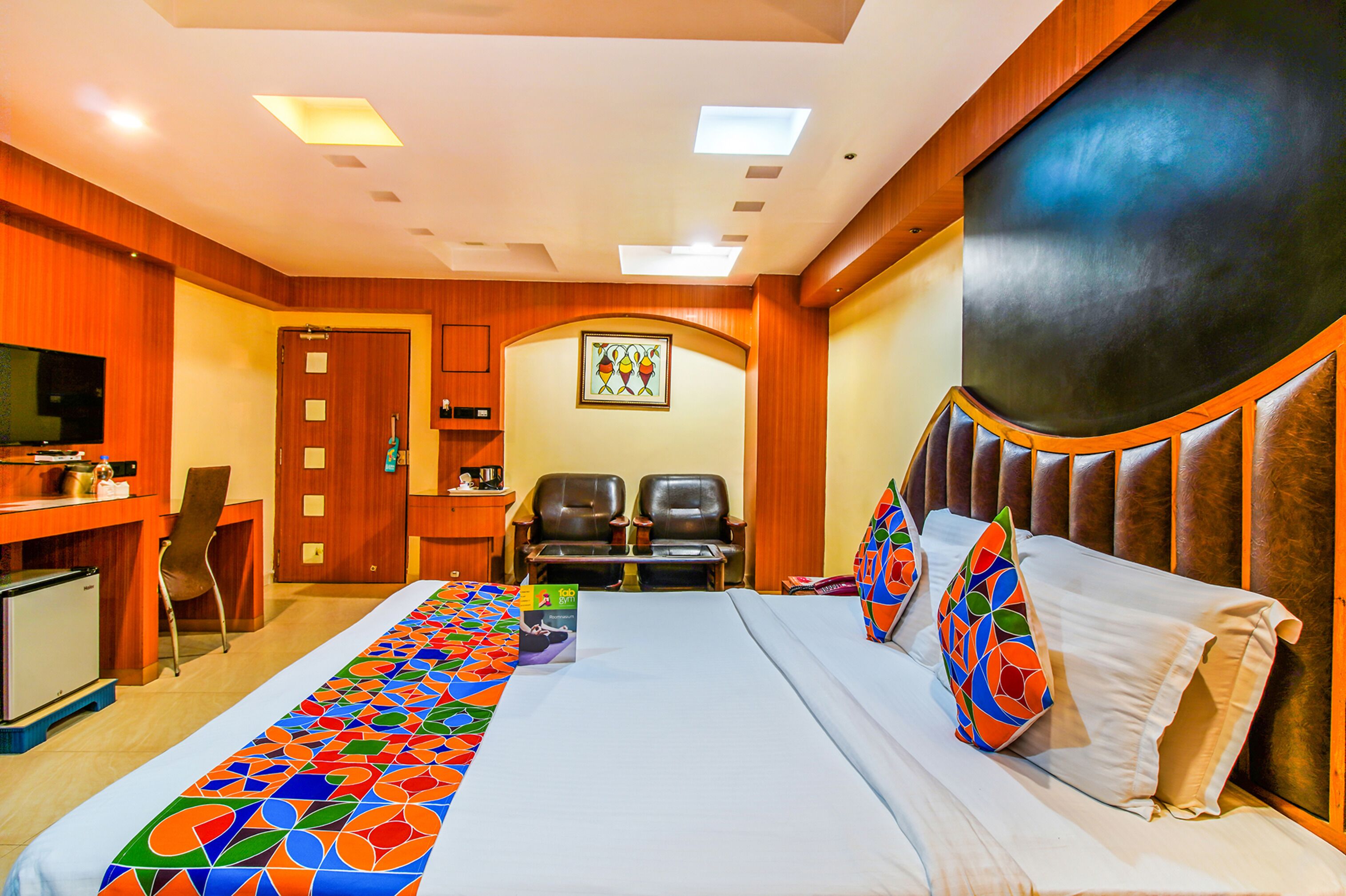 A hotel room with a bed, two chairs, a desk with a computer, and a television.