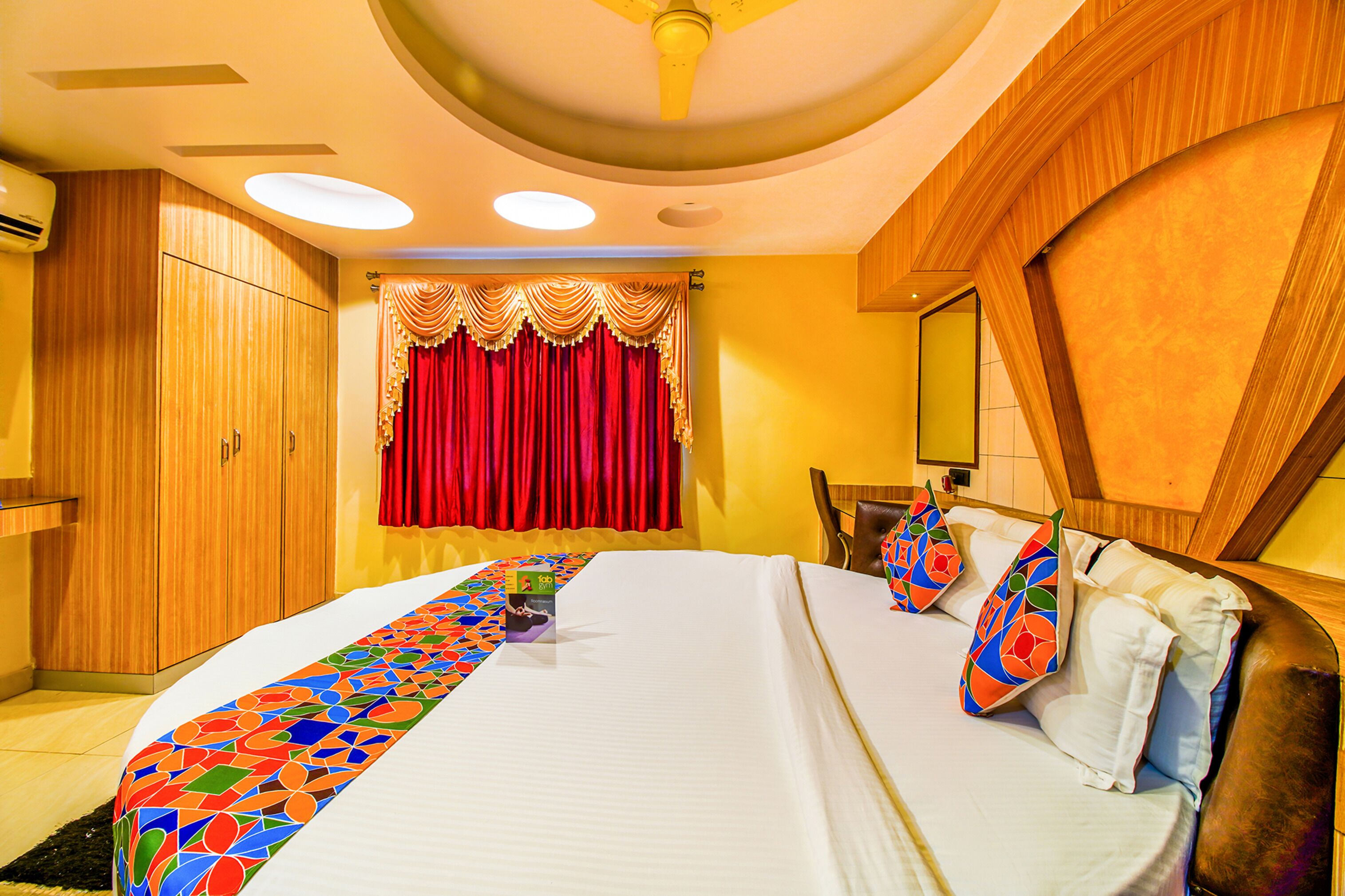 A hotel room with a large bed, a wooden wardrobe, a red curtain, and a ceiling fan.