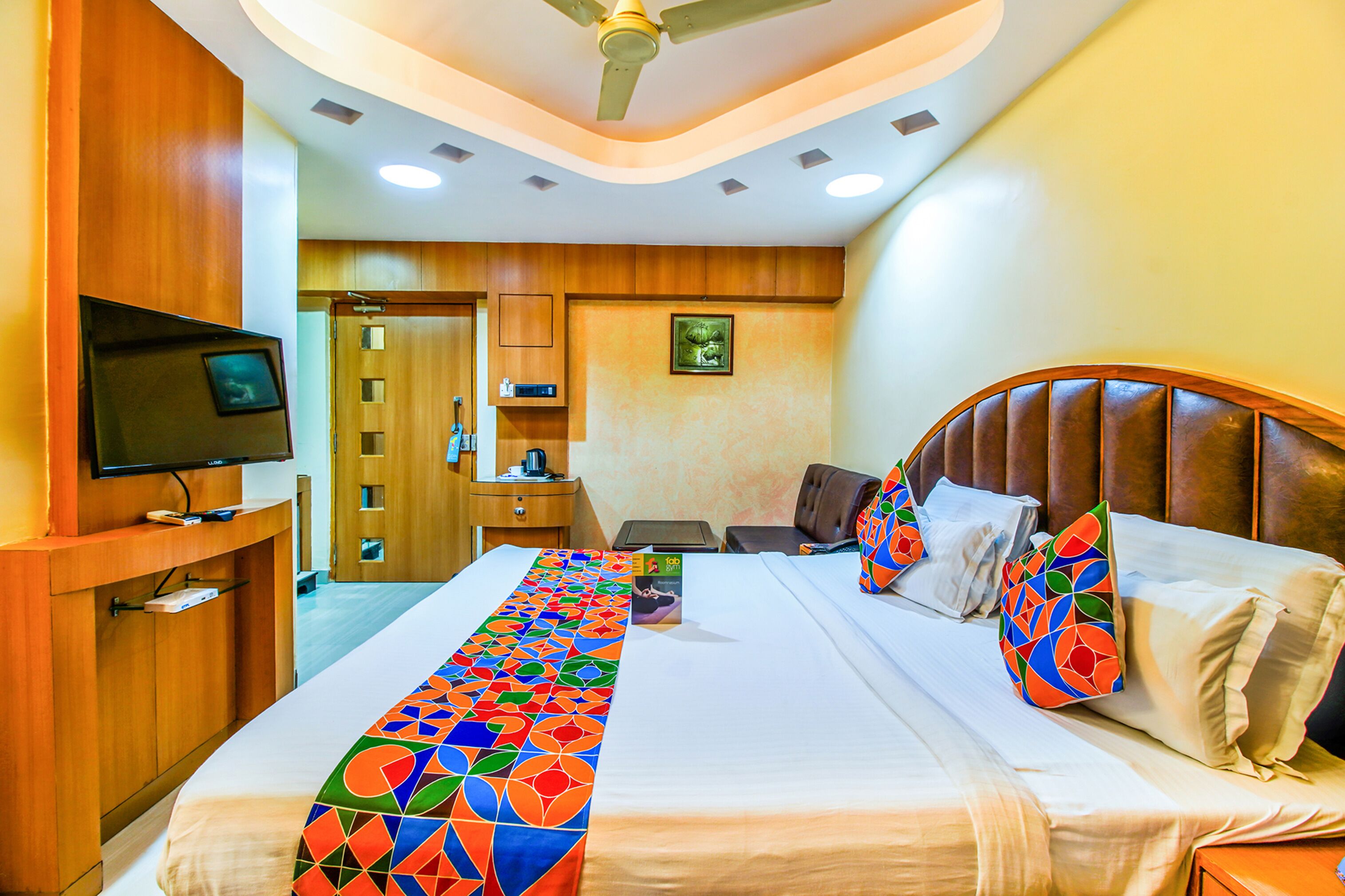 A hotel room with a large bed, a television on a wooden stand, a desk with a chair, and a wardrobe.