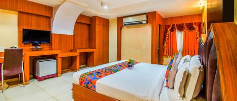 A hotel room with a bed, desk, television, air conditioning unit, and a ceiling fan.
